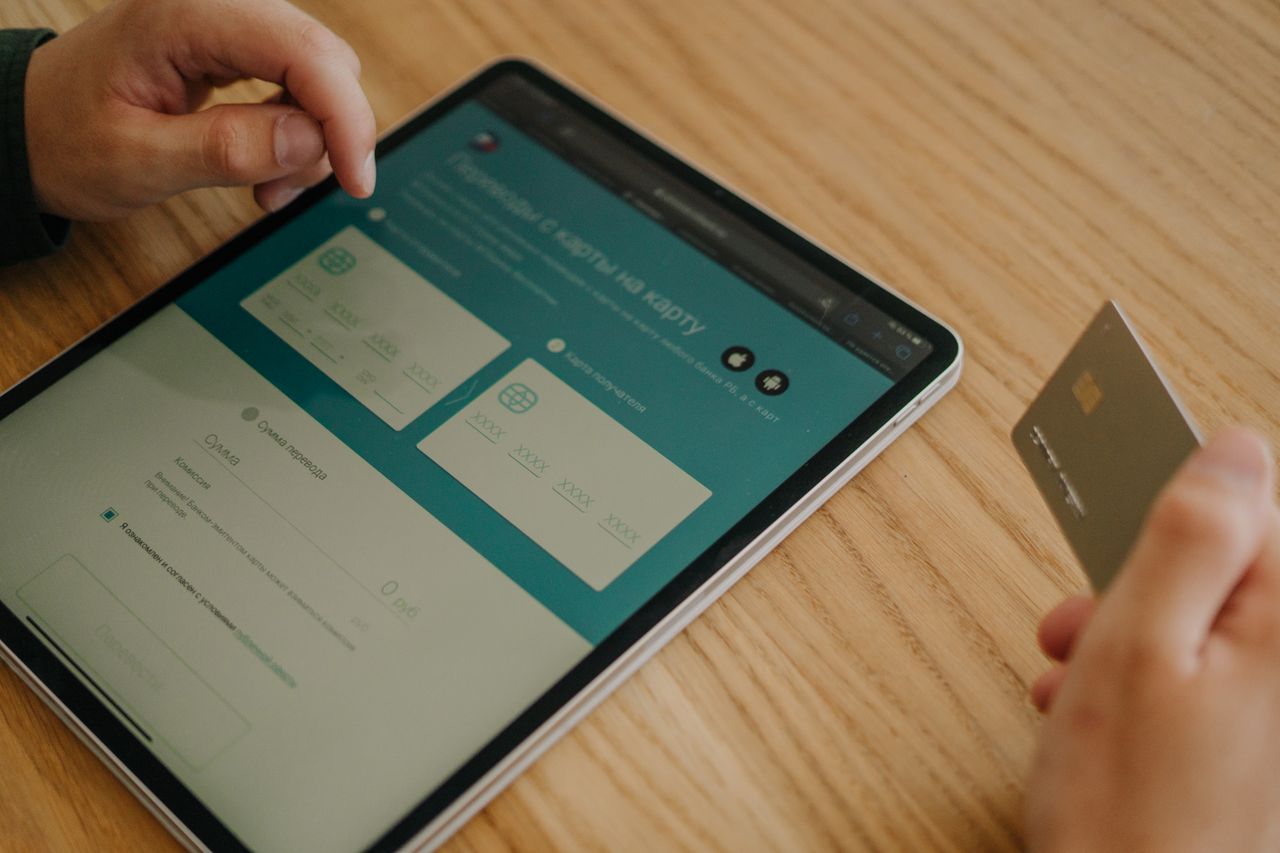About Hands making an online purchase using a tablet and credit card on a wooden table.