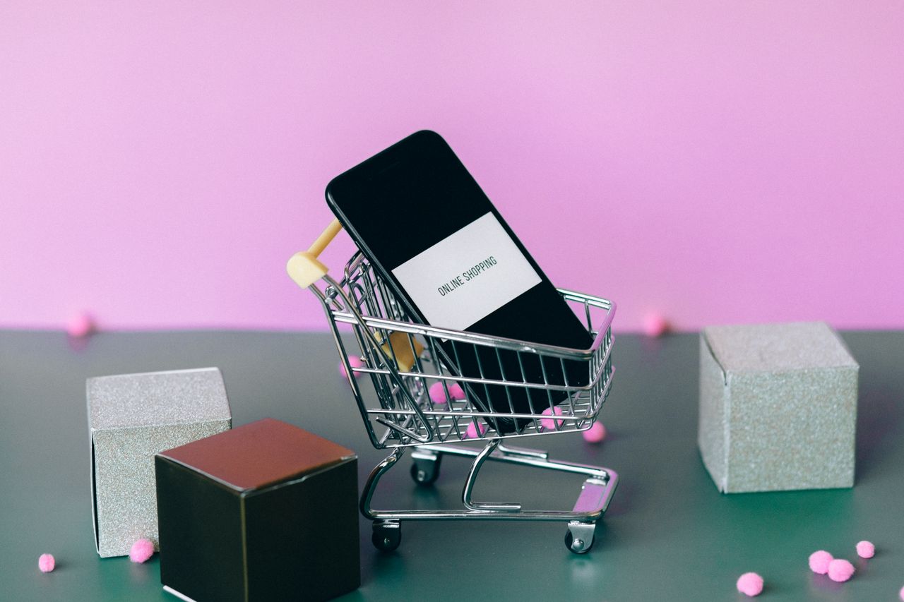 About A smartphone with a shopping cart depicting the concept of online shopping in a colorful studio setup.