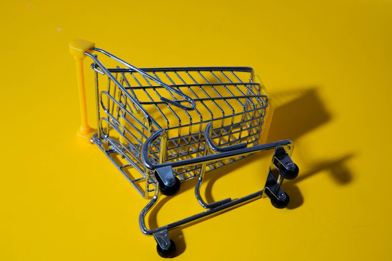 Menus Close-up of a toy shopping cart on a vivid yellow surface, casting shadows.